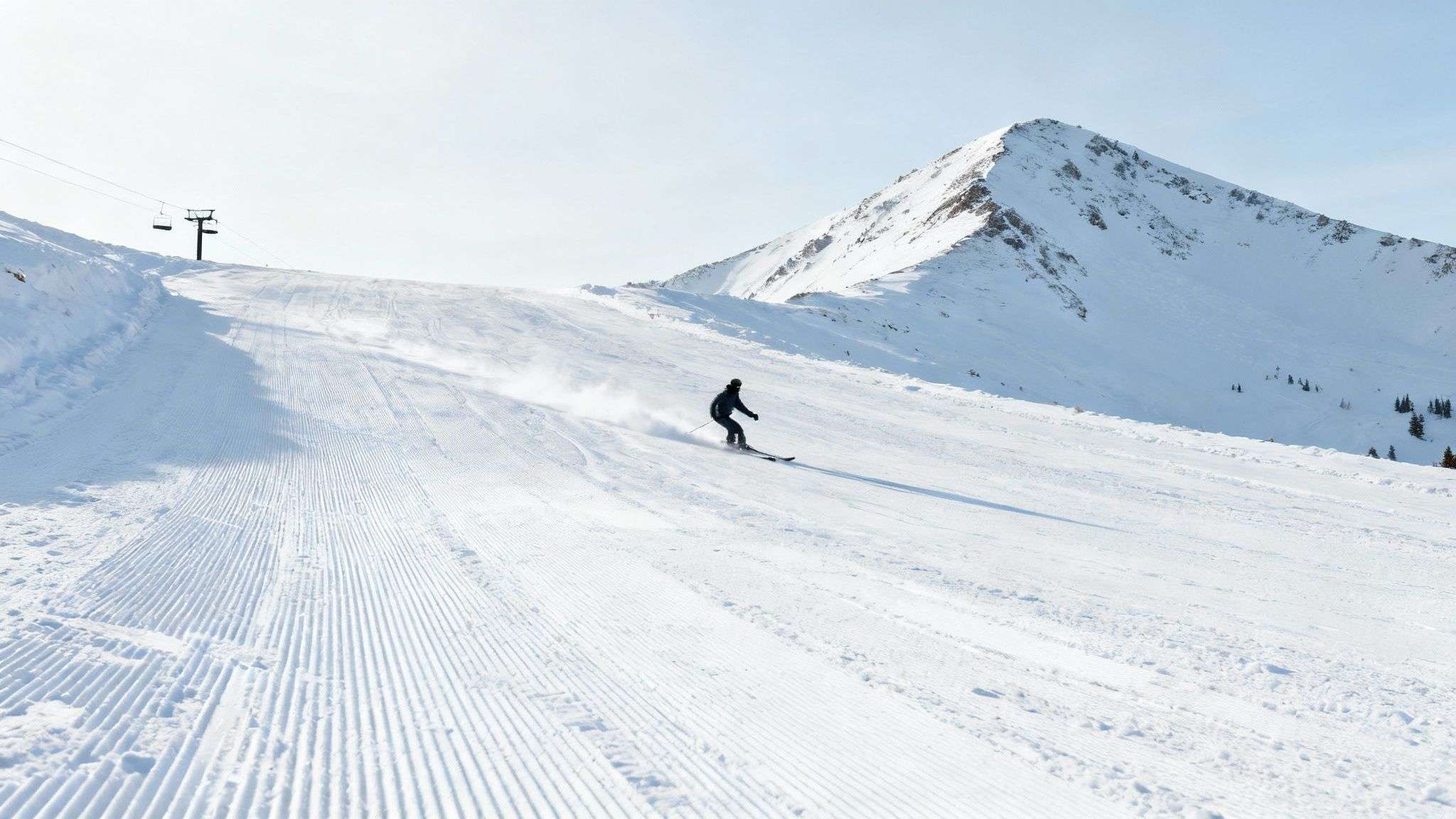 A skier carves through deep powder on a sunny day at a ski resort in Big Cottonwood Canyon.